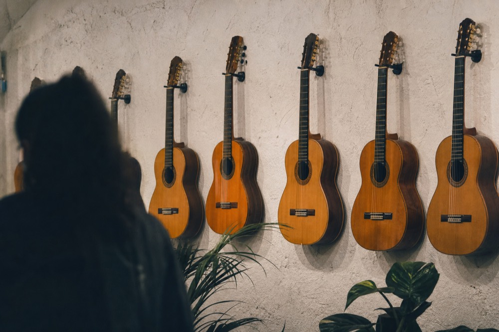 Row of old flamenco guitars hanging on a plastered wall in soft gallery lighting, no labels or text visible