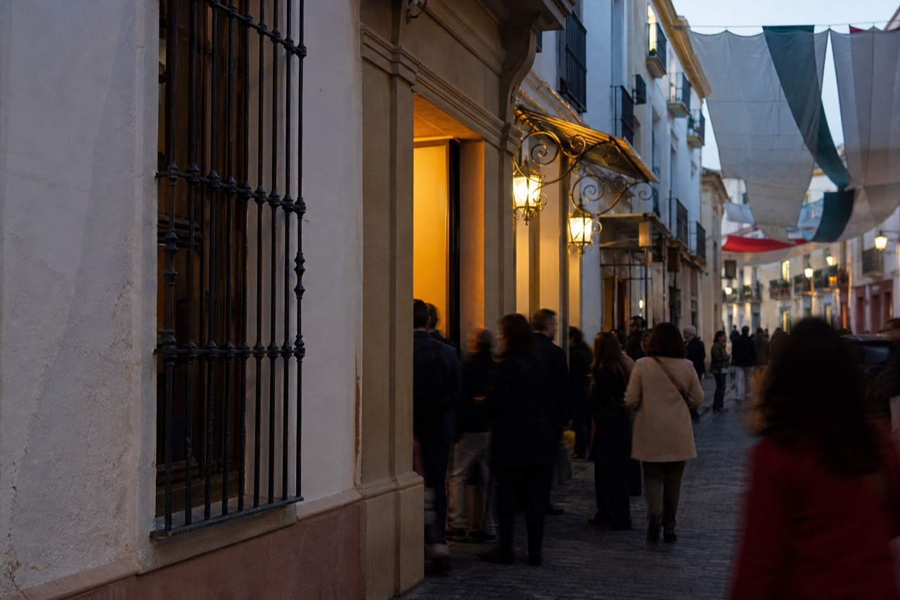 Evening crowd gathered outside a lit Seville theater doorway, festival banners hanging above the street