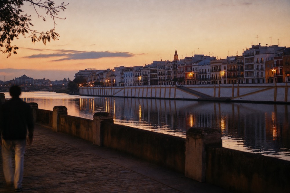 Calle Betis riverside terraces in Triana at dusk, coloured house fronts reflected in the Guadalquivir with the old town skyline opposite