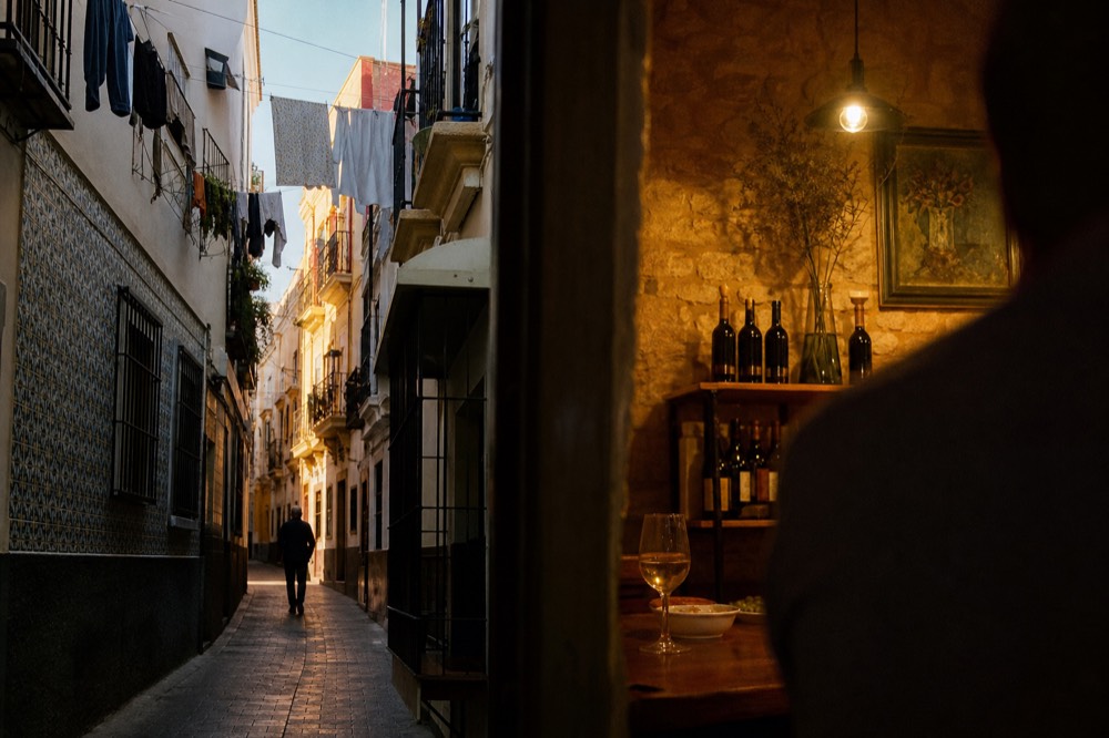 Narrow Triana street lined with painted ceramic tiles and iron balconies, washing lines overhead, late afternoon sun on one wall