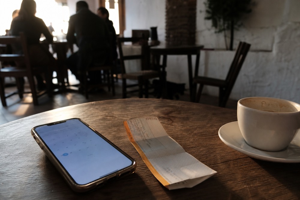 Phone screen showing a calendar and a paper ticket lying on a cafe table with a coffee cup beside them