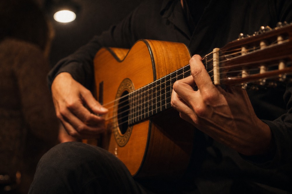Close crop of a flamenco guitarist's hands on the strings under a single warm bulb, face out of frame, dark bar behind
