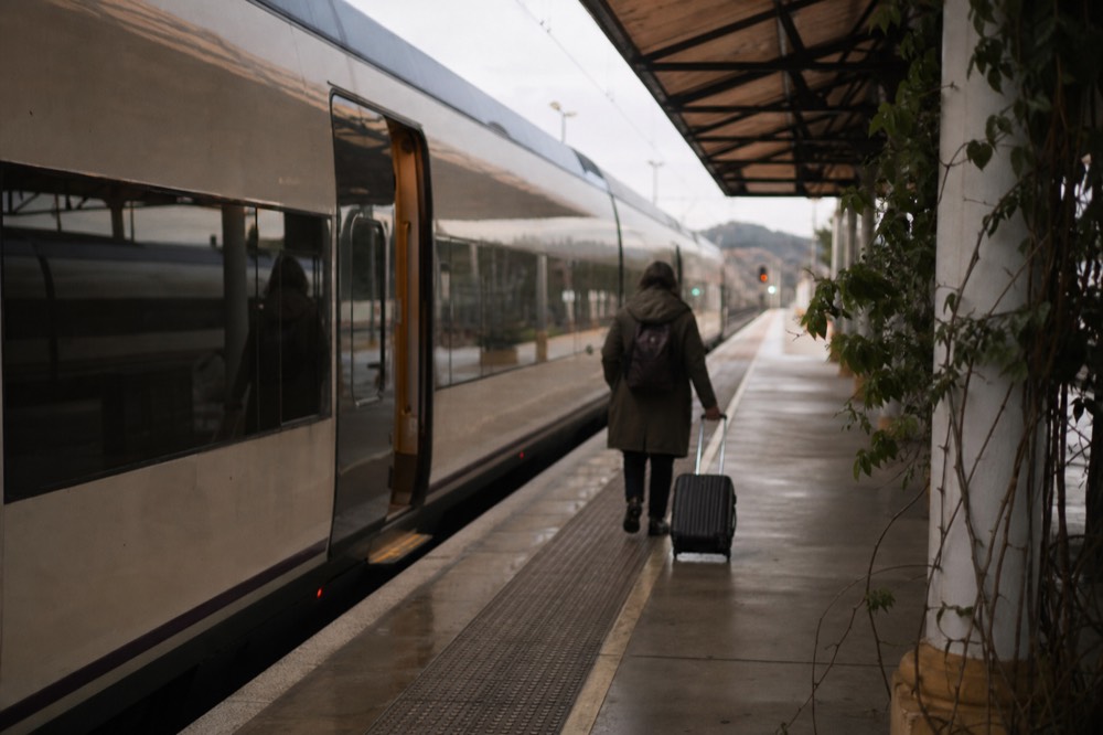 High-speed train waiting at an Andalusian platform in early morning light, a traveller with a small case walking towards the open door